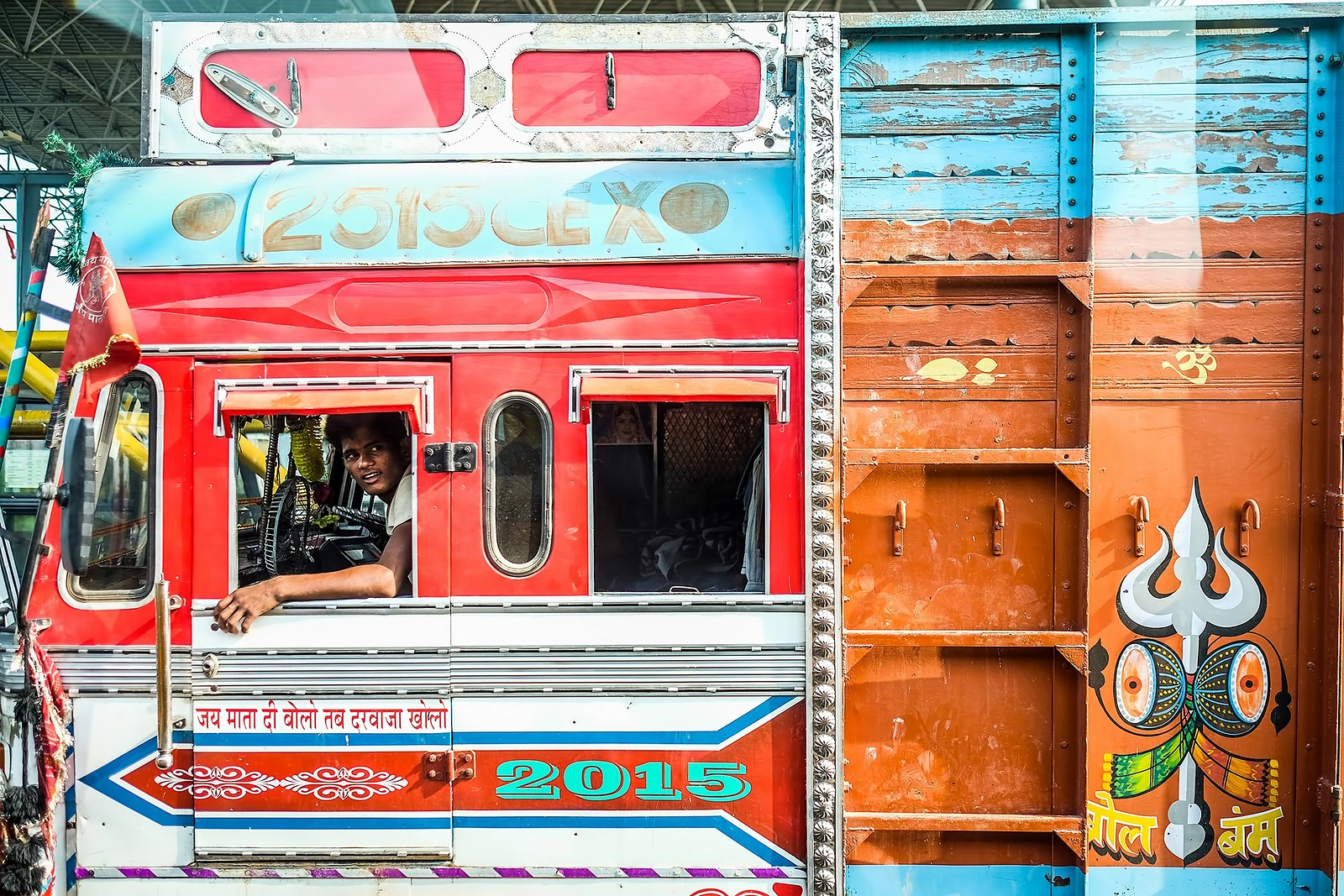 A driver looking out of the cab of a brightly painted Indian lorry