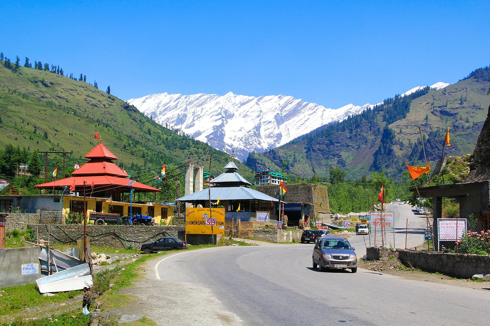 Snow-covered peaks above a green valley and a mountain road near Manali