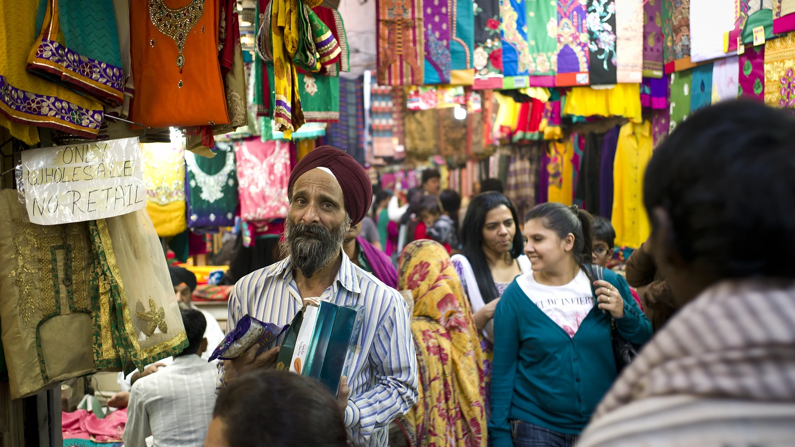 Shoppers in a crowded cloth market hung with bright fabrics