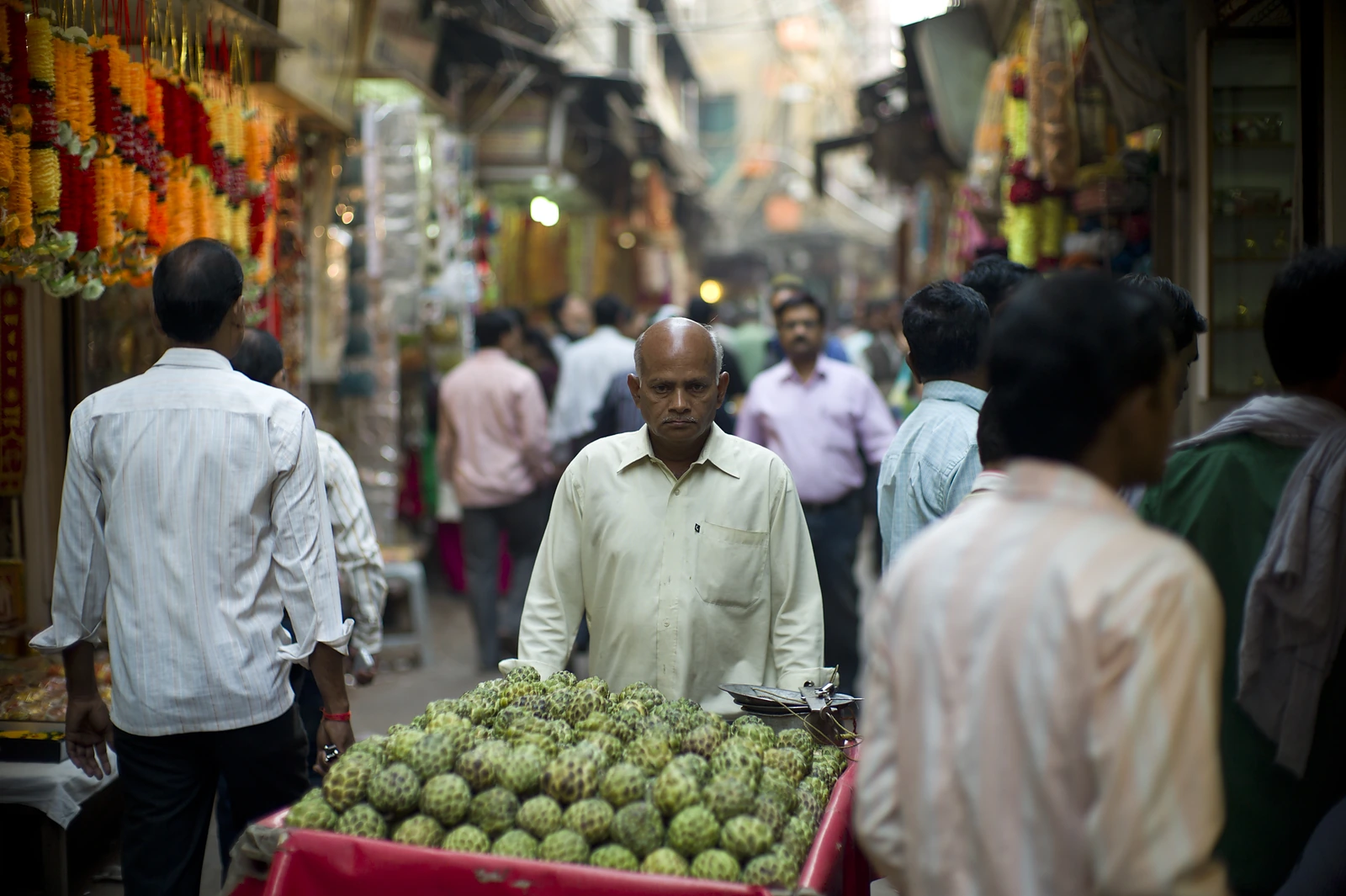 Un marchand poussant une charrette de pommes cannelle dans une ruelle animée du vieux Delhi