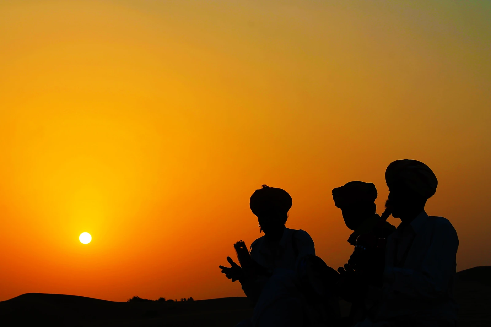 Musicians in turbans silhouetted against a desert sunset in Rajasthan